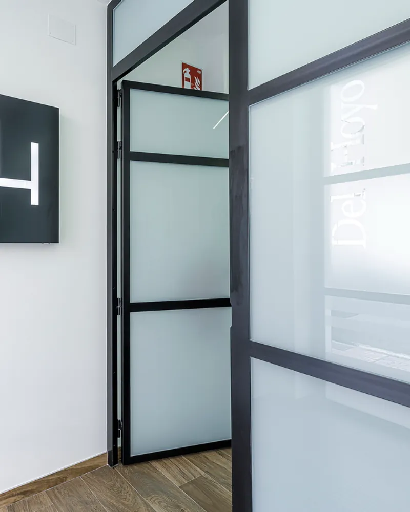 El logotipo DH sobre panel negro, junto a la mampara