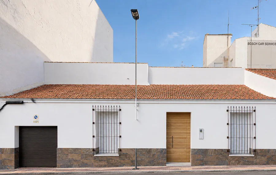 Fachada encalada de Villa Familia Vera con el zócalo de piedra, la puerta de madera y las rejas